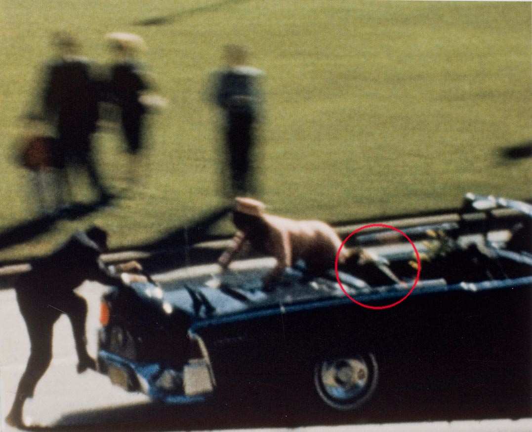 Un agente sale sull'auto presidenziale subito dopo l'uccisione di Kennedy che giace riverso (nel cerchio rosso).